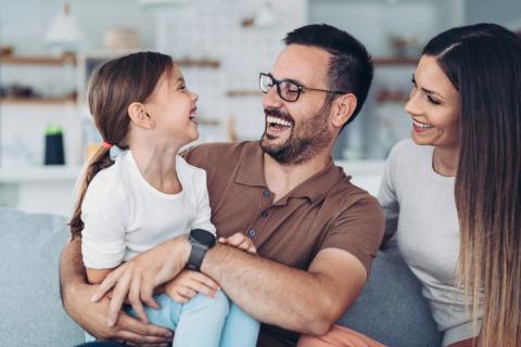 Mother, father and child sitting on couch, laughing