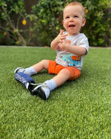 Toddler with leg braces, sitting on grass