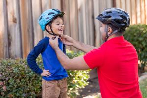 Parent adjusting bicycle helmet on boy