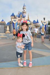 Two young girls smiling in front of a Disney castle