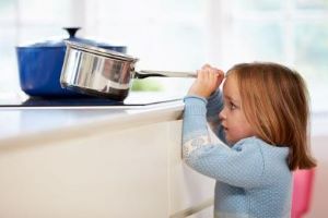 Young girl pulling a pot off the stove