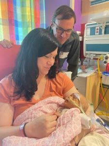Mother holding newborn in hospital with father looking over her shoulder
