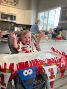 Smiling baby in highchair, arms up, surrounded by Happy Birthday decorations