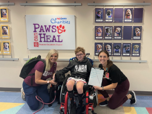 Two providers and dog pose with boy in wheelchair