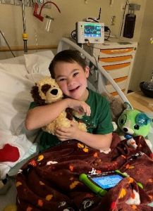 Boy in hospital bed, hugging stuffed dog