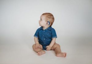 Infant sitting on floor showing hearing aid on left ear