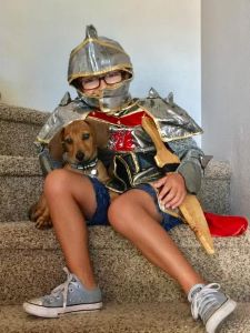 Boy dressed as a knight, sitting on stairs with small dog