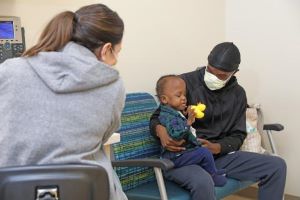 Masked father holding toddler in exam room