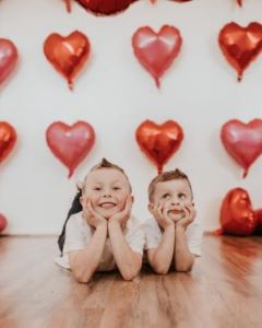 Two boys posing in front of wall of red hearts