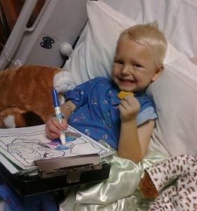 Toddler boy coloring in hospital bed and eating a cookie