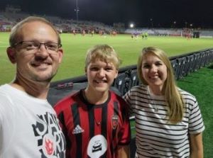 Parents posing with teen son in front of soccer field