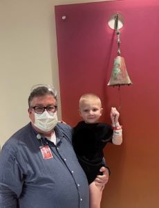 Masked doctor holding toddler, ringing a bell