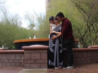 Father, mother and young child embracing, looking at pregnant belly