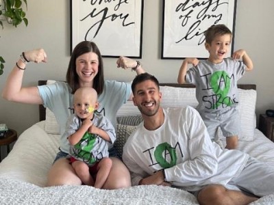 Family of 4 on bed, flexing their muscles