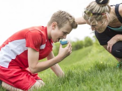 Boy using inhaler, with mom crouching nearby