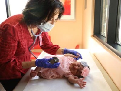 Masked doctor examining infant in pink
