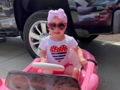 Toddler wearing red heart sunglasses in pink toy car