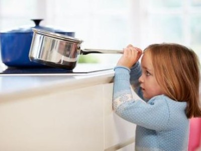 Young girl pulling a pot off the stove
