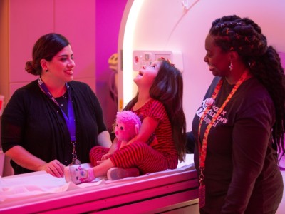 Little girl on MRI with two female providers smiling next to her