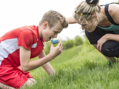 Boy using inhaler, with mom crouching nearby