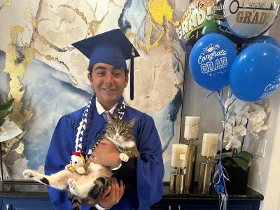 Teen boy in blue graduation cap and gown smiling while holding cat