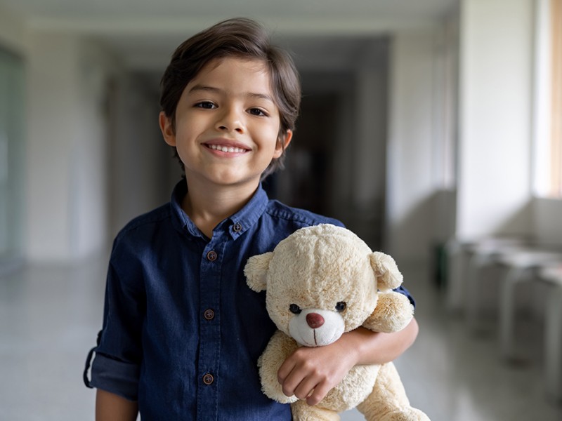 Boy smiling, standing in hospital hallway with teddybear