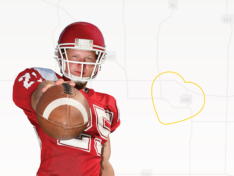 Boy in red uniform and helmet holding football