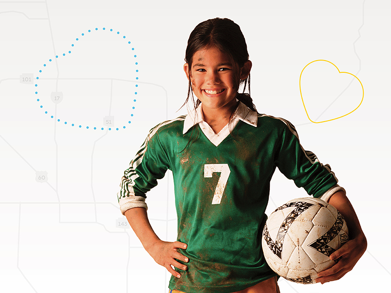 Girl in green uniform smiling and holding soccer ball