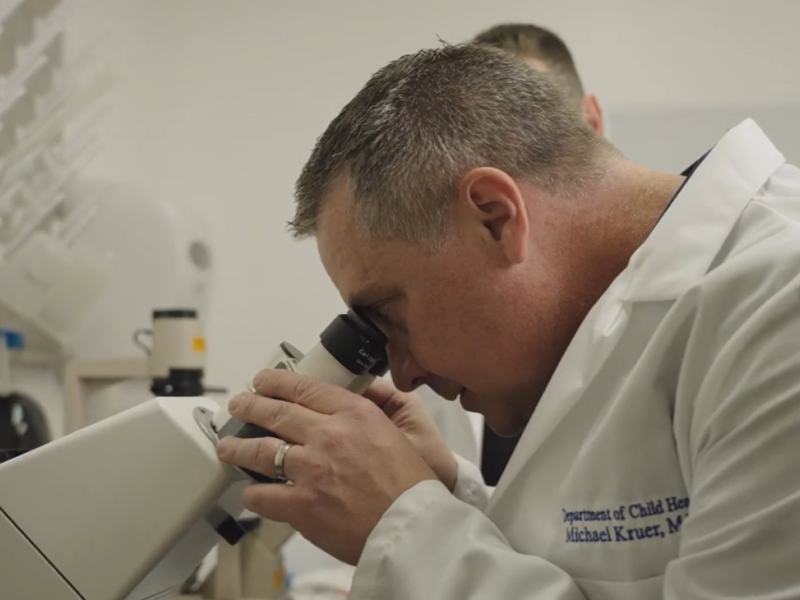 Researcher in white lab coat looking into microscope