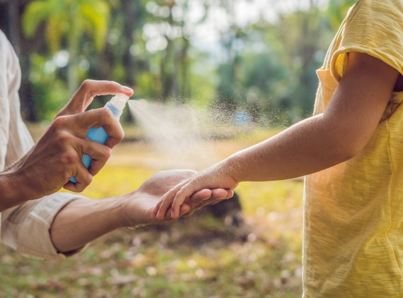 Parent spraying repellant on child's arm