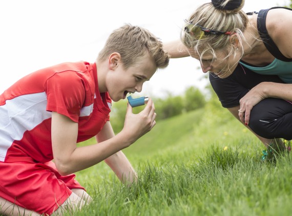 Boy using inhaler, with mom crouching nearby