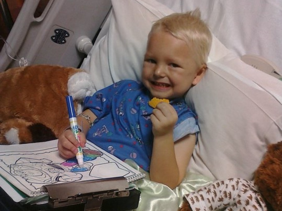 Toddler boy coloring in hospital bed and eating a cookie