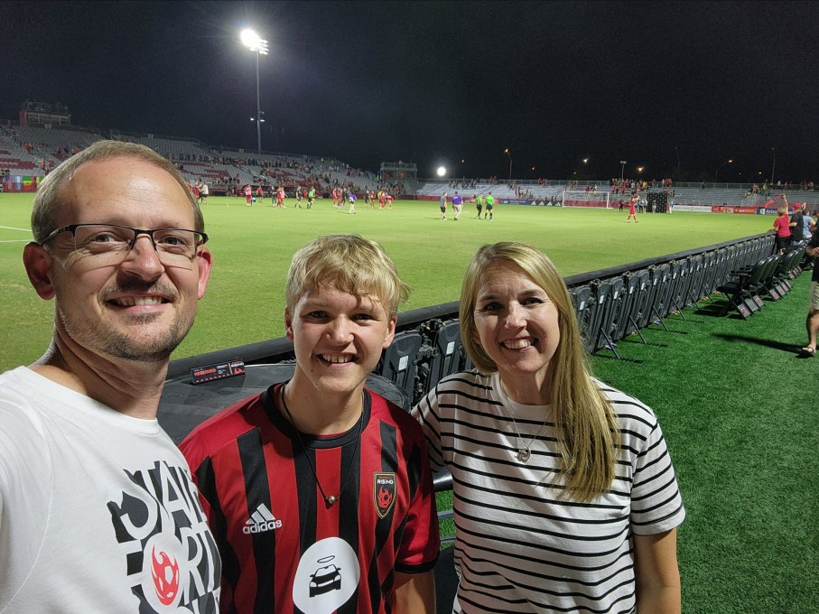 Parents posing with teen son in front of soccer field