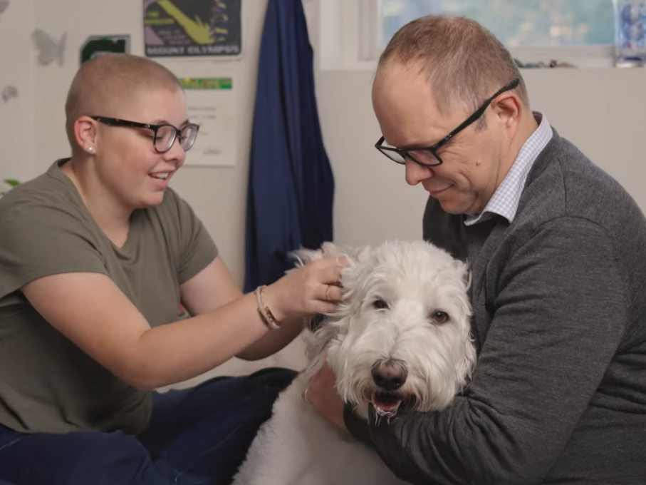 Teen girl and parent petting smiling white dog