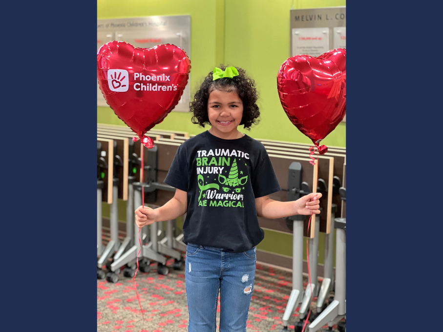 Girl in TBI shirt holding heart balloons