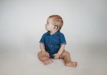 Infant sitting on floor showing hearing aid on left ear