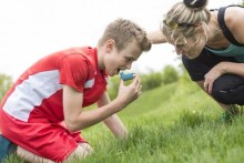 Boy using inhaler, with mom crouching nearby