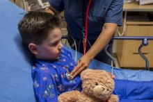 Child in hospital bed, getting checked by provider