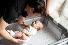 Father putting baby down into cot