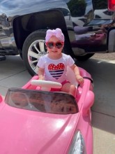 Toddler wearing red heart sunglasses in pink toy car