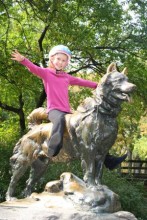 Girl wearing helmet, sitting on dog statue