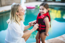 Woman and little girl in life jacket at pool