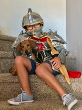 Boy dressed as a knight, sitting on stairs with small dog