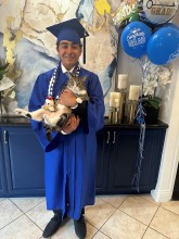 Teen boy in blue graduation cap and gown smiling while holding cat