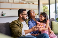 Mom, dad and girl sitting on couch and smiling